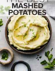 A large plate full of creamy mashed potatoes with a garnish of fresh parsley.