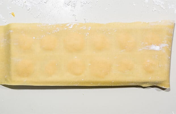 A sheet of ravioli dough covering the filled ravioli mold.