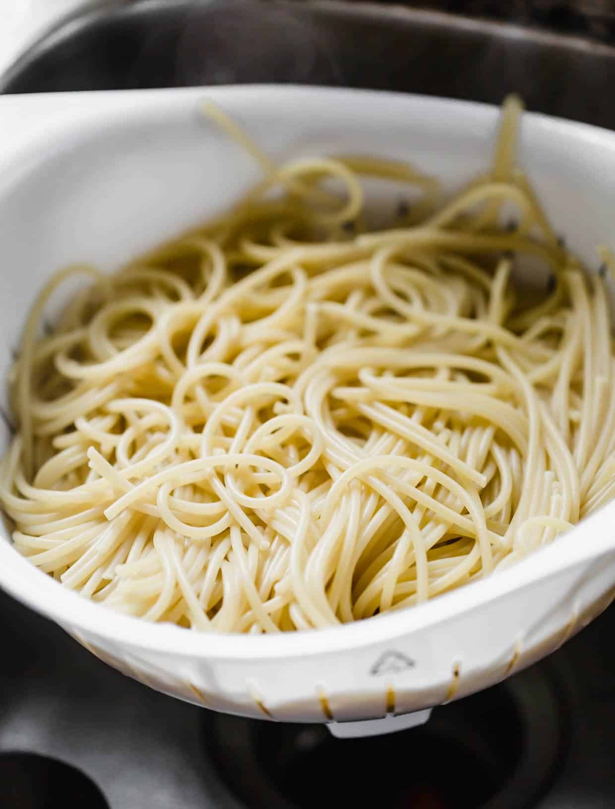 Spaghetti noodles in a white strainer.