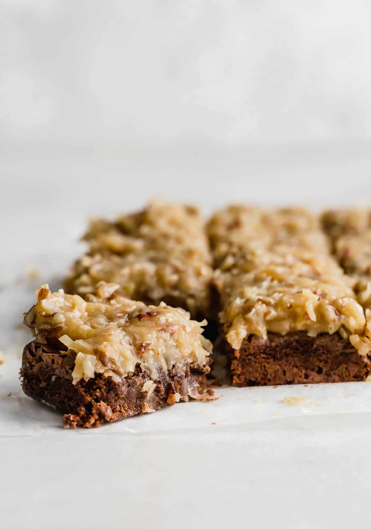 A square of German Chocolate Brownies topped with coconut pecan frosting against a white background. 