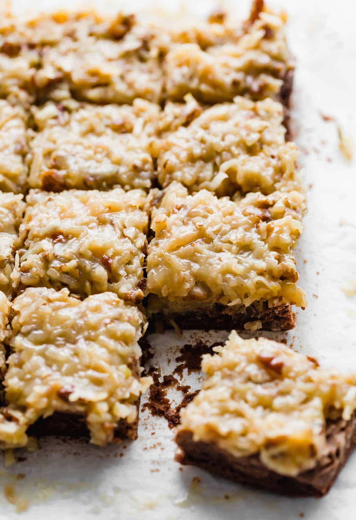 German Chocolate Brownies topped with a coconut pecan frosting, on a white background.