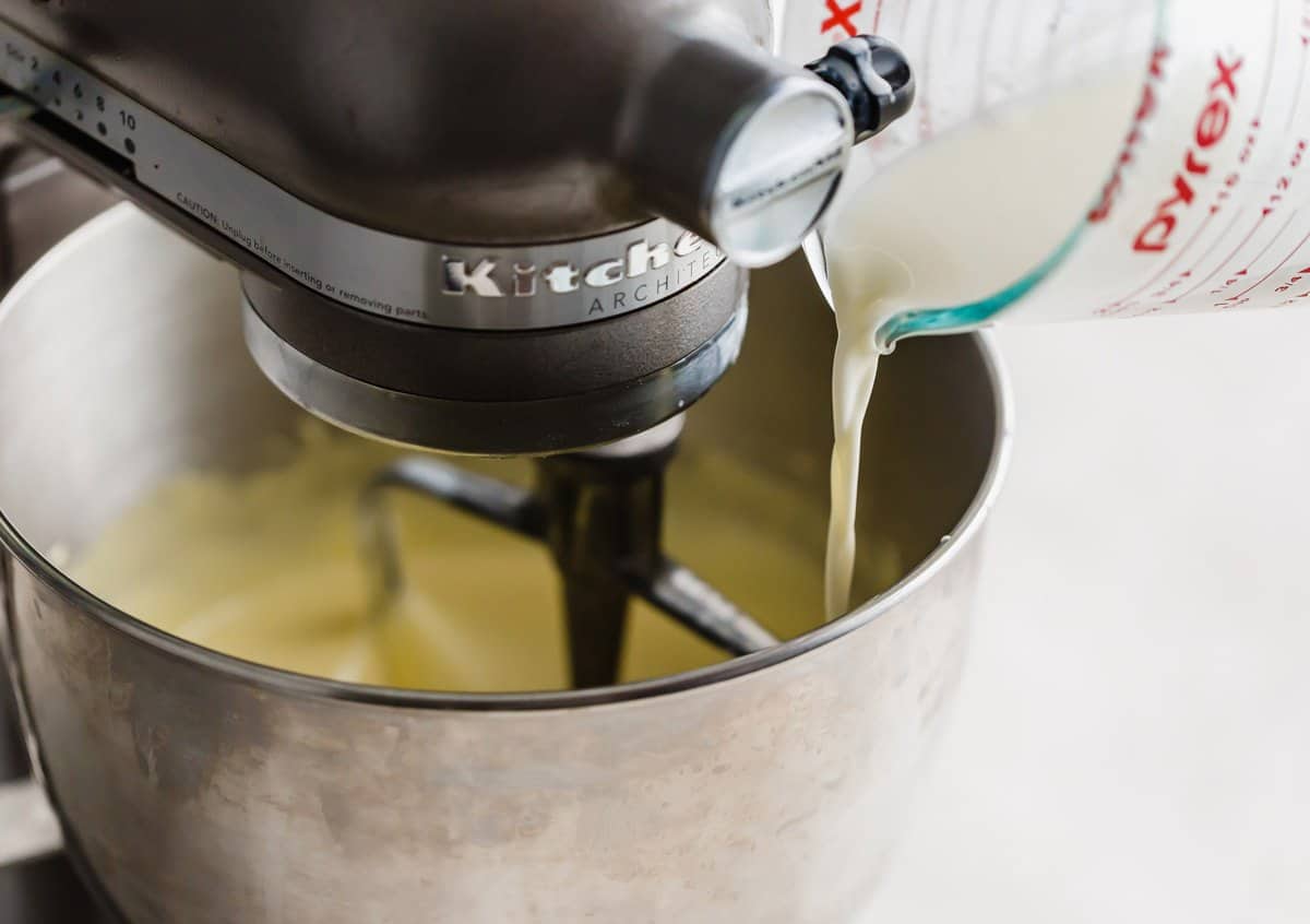 A white hot liquid being poured into a Homemade Vanilla Ice Cream custard mixture in a stand mixer.