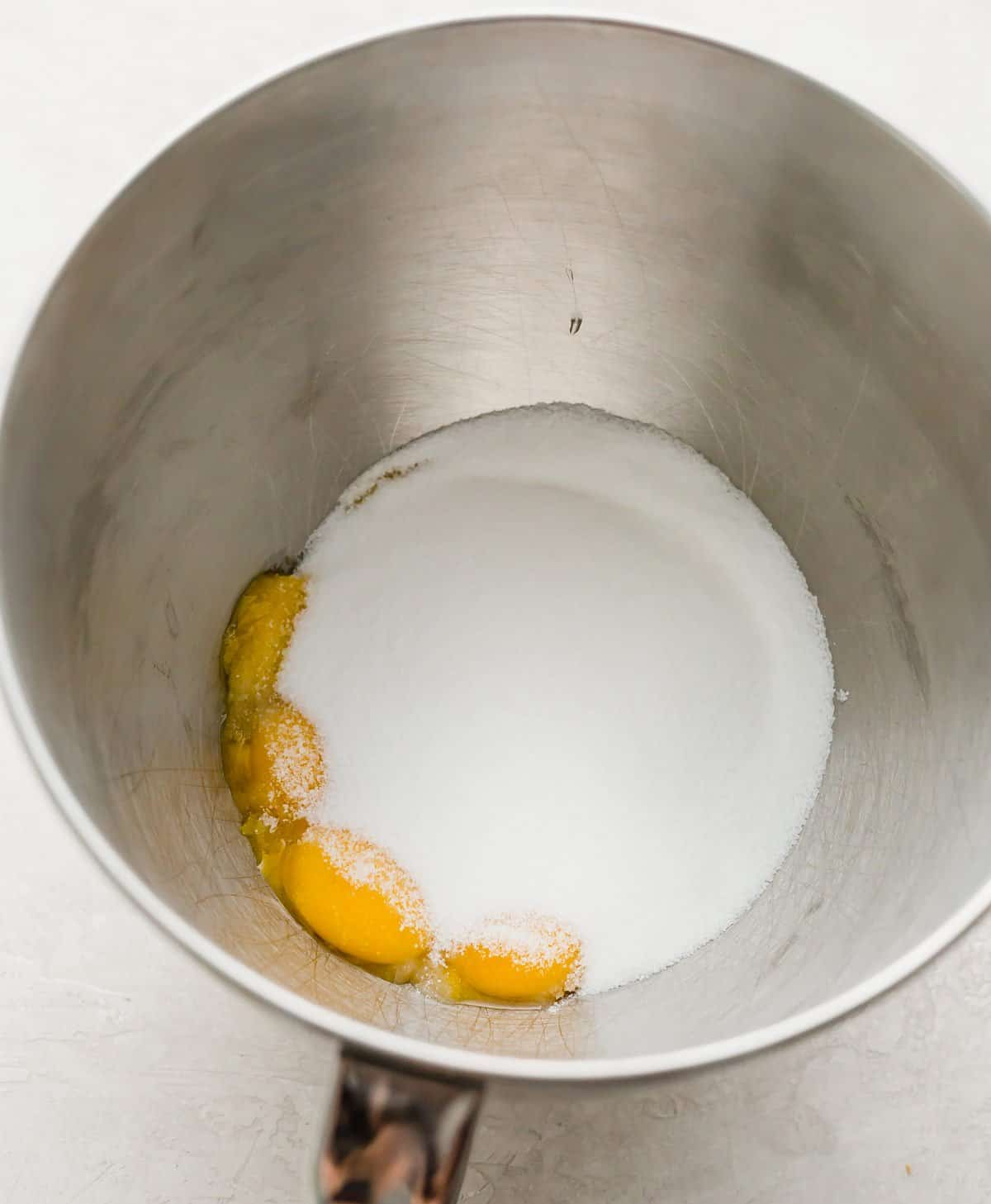 Sugar and egg yolks in a metal mixing bowl.