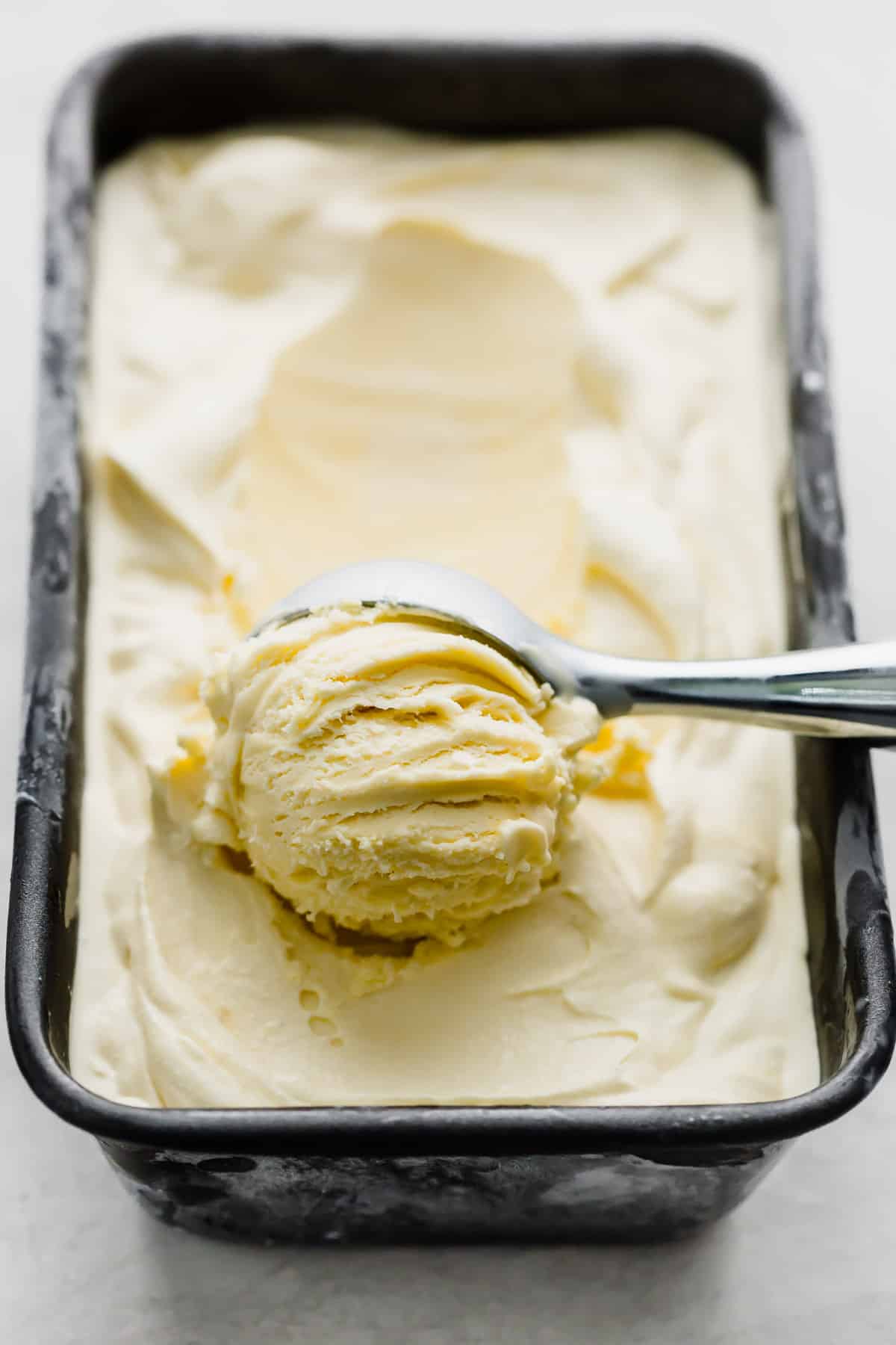 Homemade Vanilla Ice Cream in a bread pan with an ice cream scooping spooning out a portion.