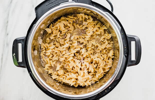 Overhead view of an instant pot with browned beef, egg noodles, and additional ingredients for making instant pot beef stroganoff.