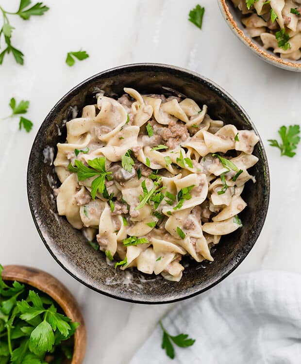 A black bowl full of beef stroganoff and garnished with fresh parsley.