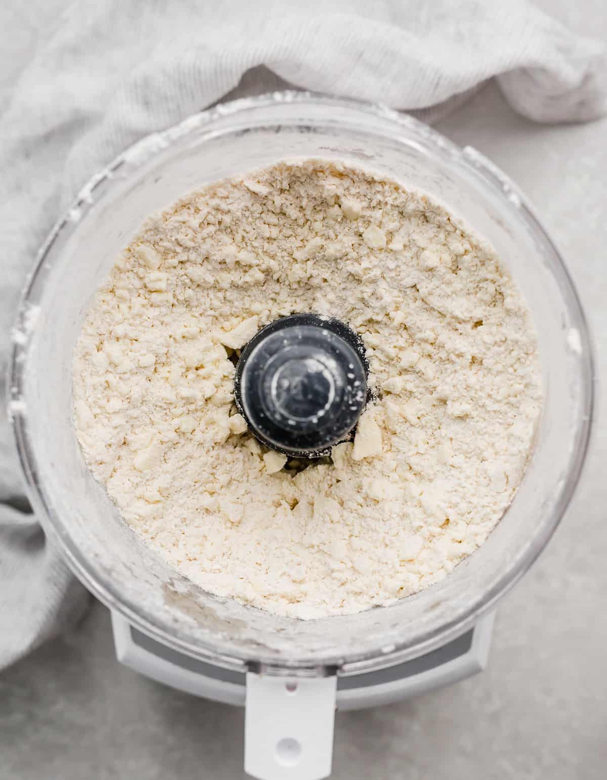 A food processor with flour and mixed butter in it, to appear like coarse meal.