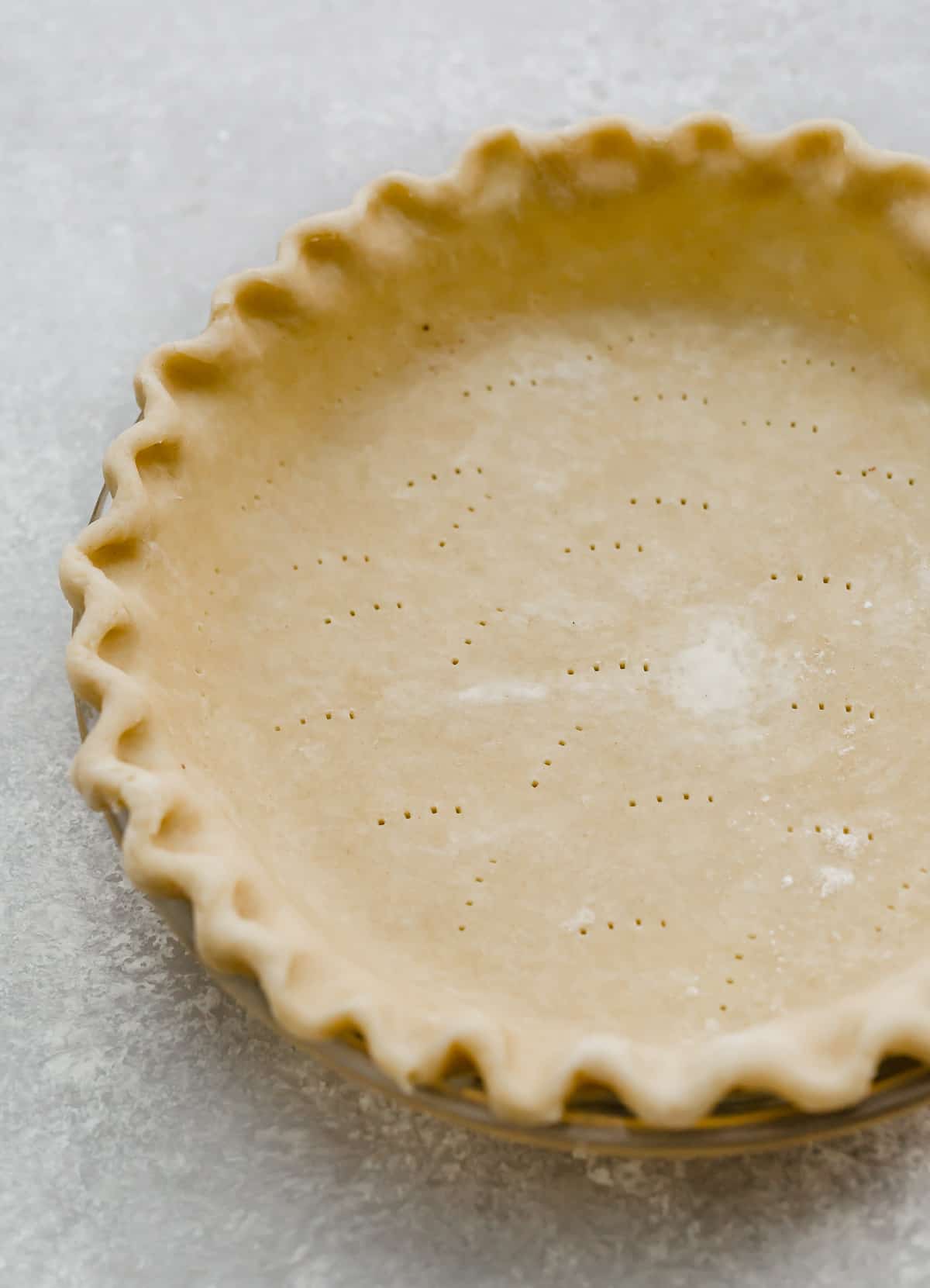 A fluted Food Processor Pie Crust with fork tines poked into the bottom of the unbaked crust.