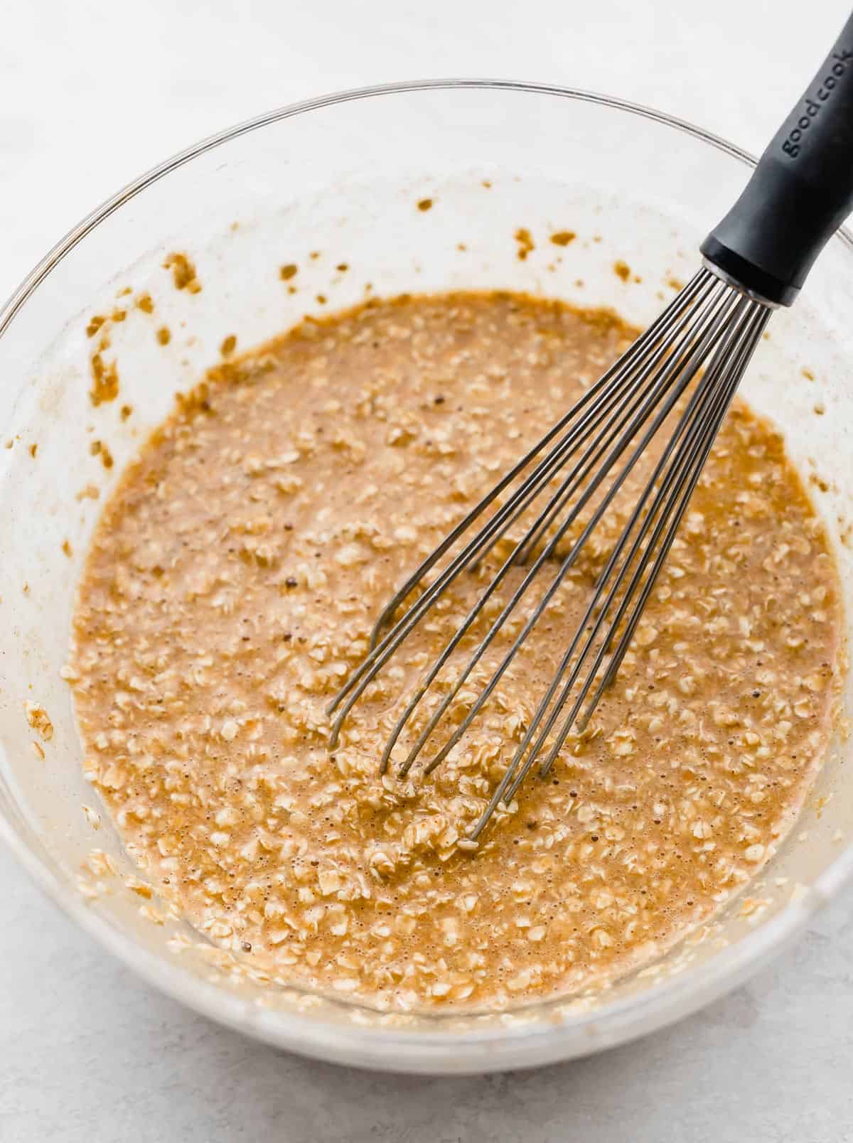 A whisk stirring Pumpkin Baked Oatmeal Cups batter in a glass bowl.