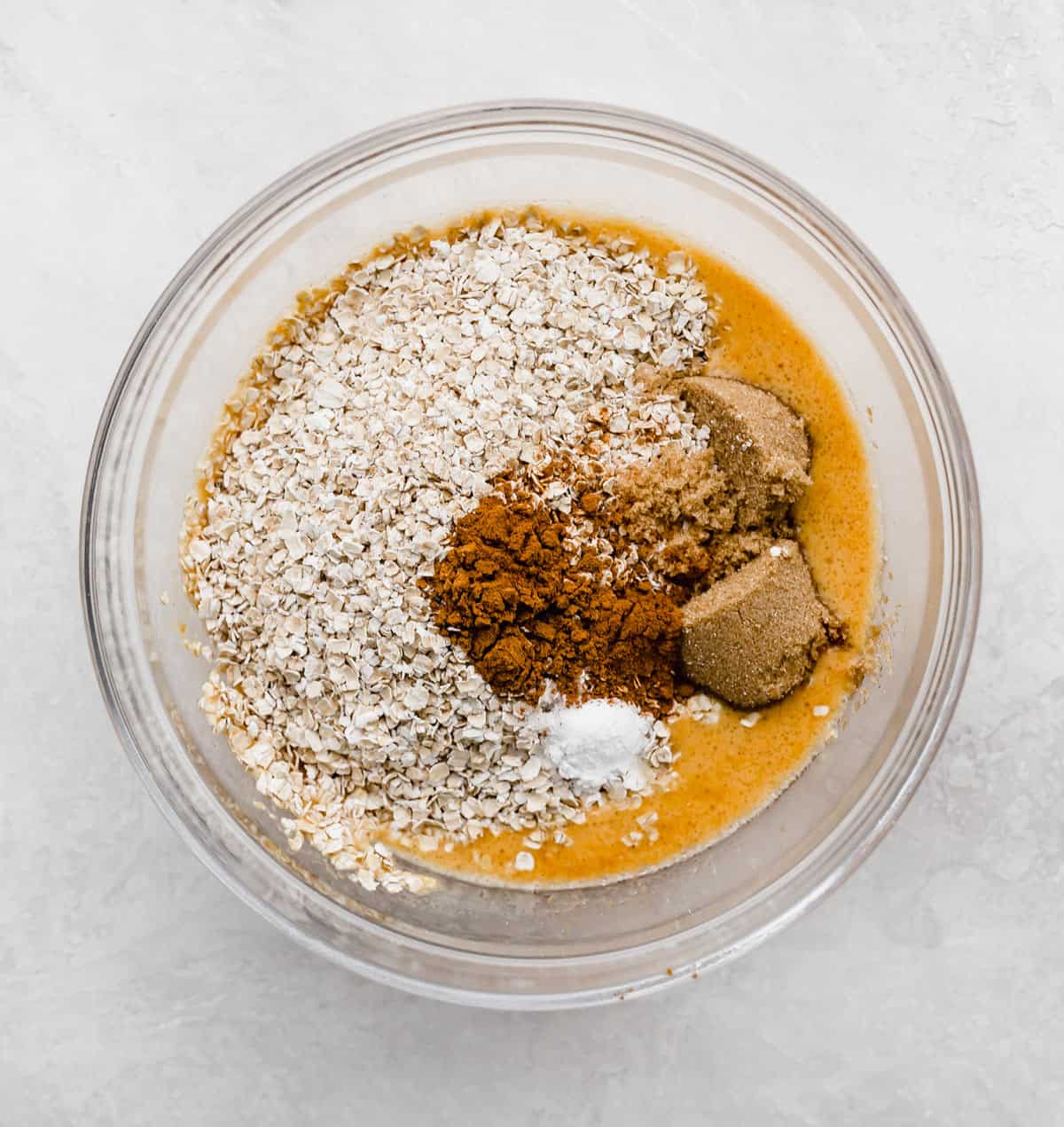 A glass bowl with oats, brown sugar, pumpkin puree and baking powder in it.
