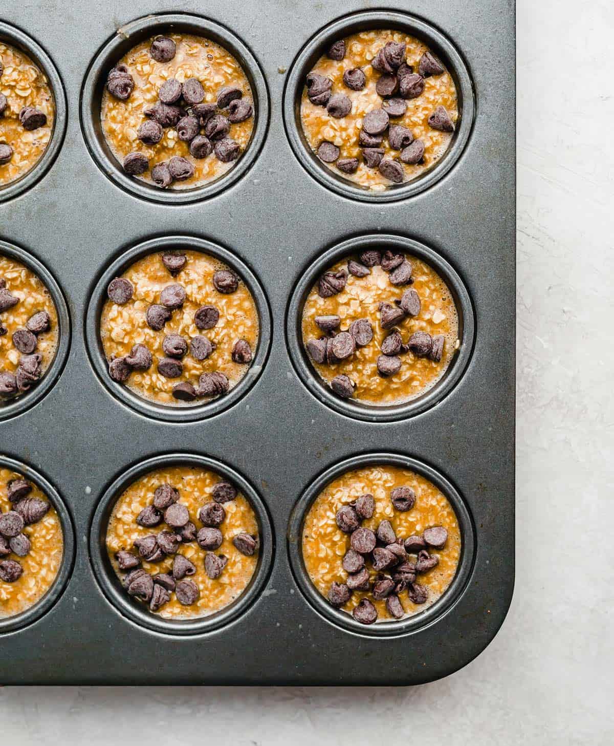 Pumpkin Baked Oatmeal Cups batter topped with chocolate chips in a muffin tin.
