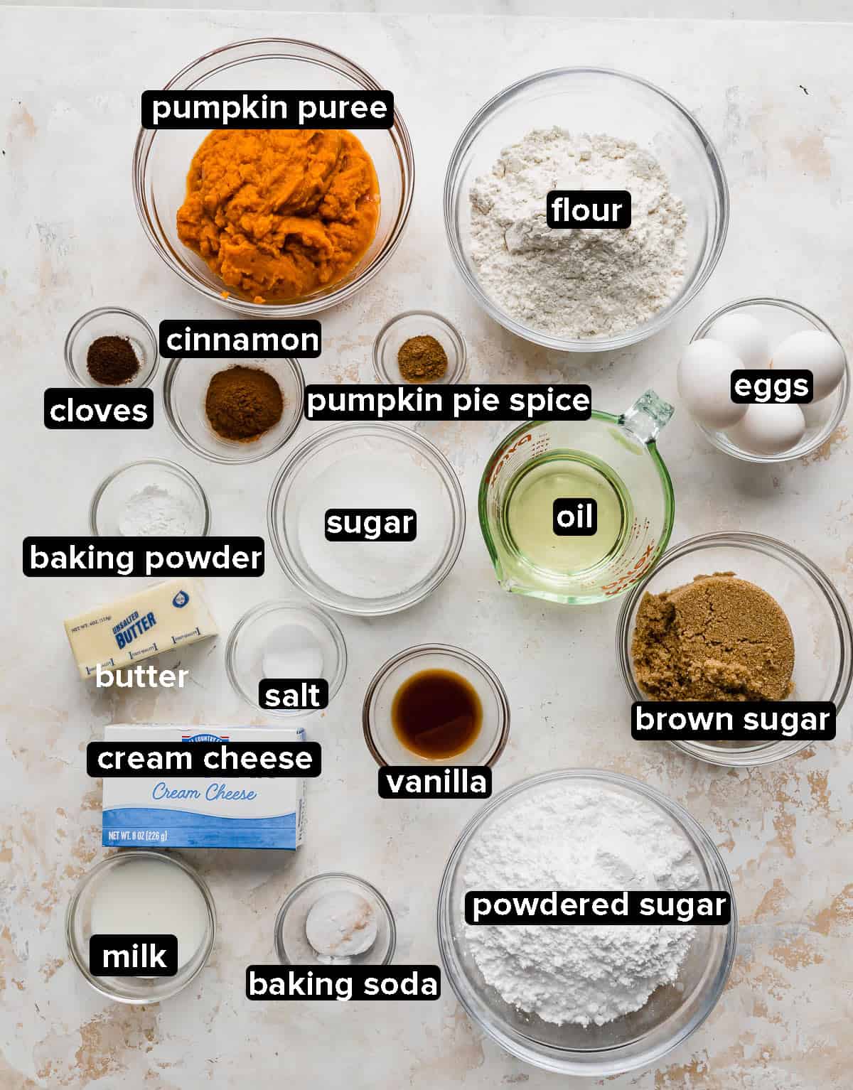 Pumpkin Layer Cake ingredients in small glass bowls on a textured white background.