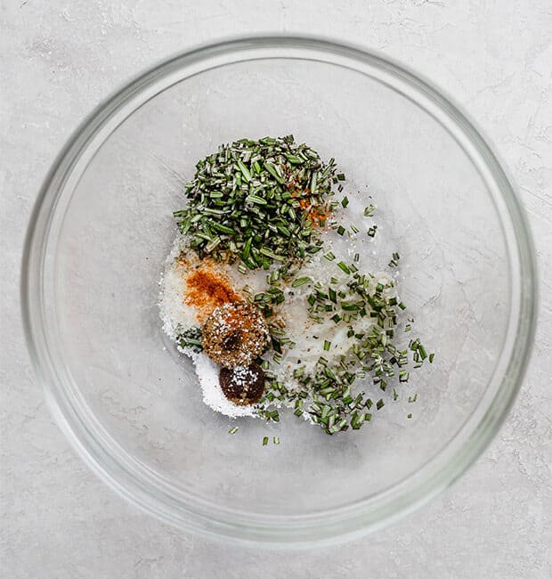 A glass bowl with fresh rosemary, cayenne, salt, and melted butter.