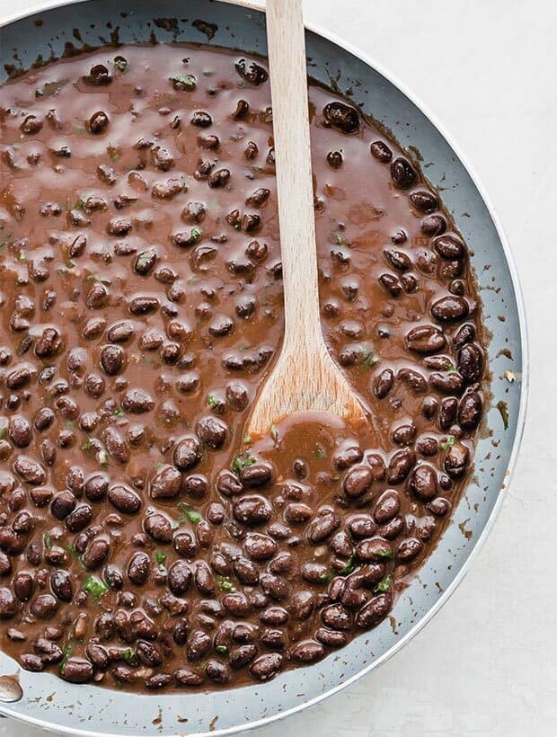 A wooden spoon stirring a pan of homemade Cafe Rio black beans.
