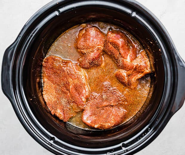 A slow cooker with pork shoulder pieces, green salsa, and Coca Cola, for making Cafe Rio sweet pork.