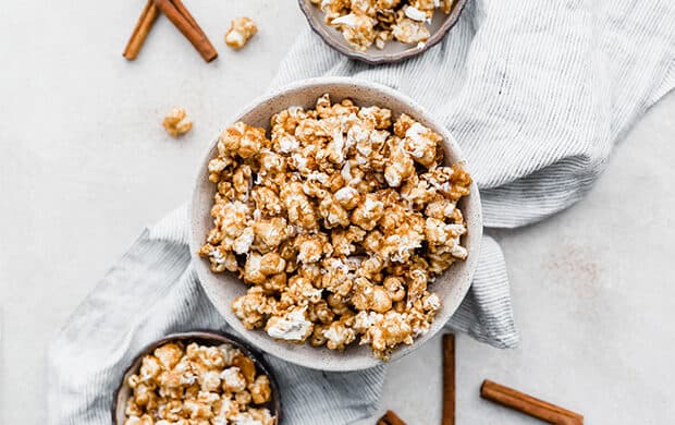 A large bowl of Cinnamon Roll Popcorn with cinnamon sticks next to the bowl.