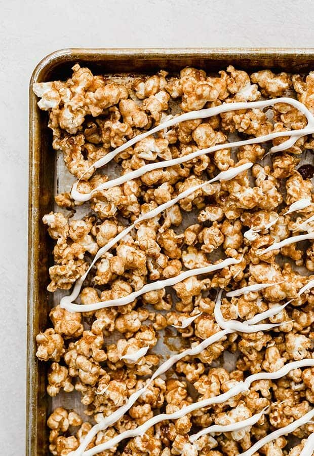 A baking sheet full of Cinnamon Roll Popcorn drizzled with white chocolate.