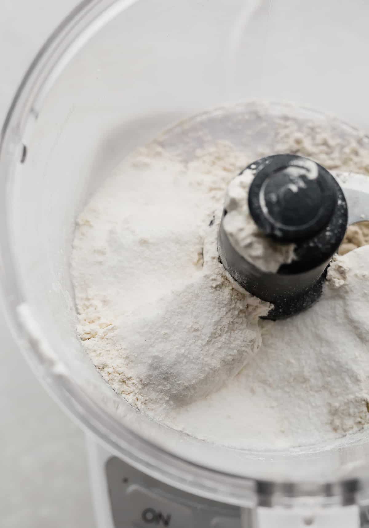 A food processor with flour and sugar in it.