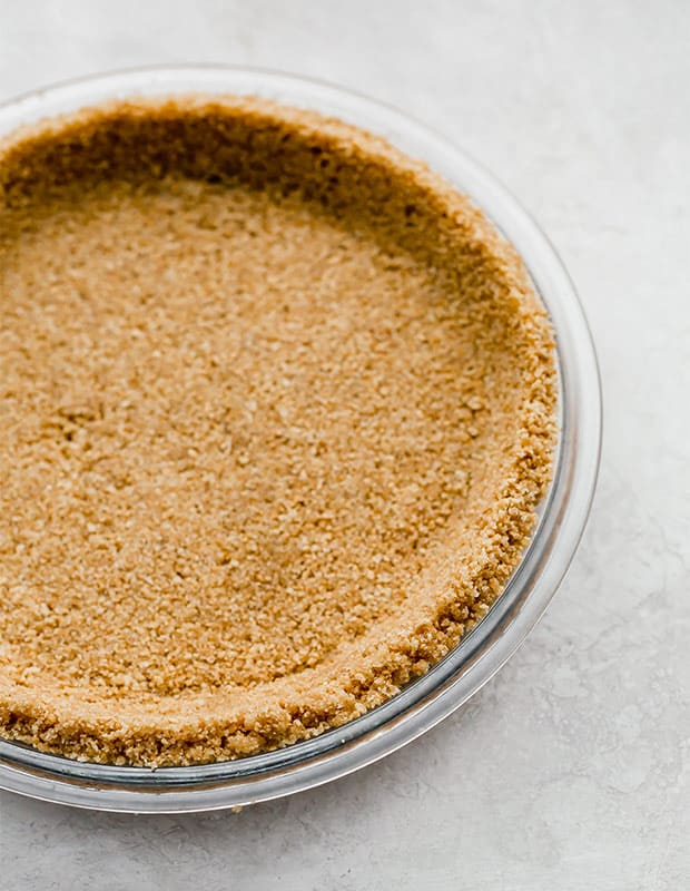 Side angle of a perfectly made graham cracker crust in a pie plate.