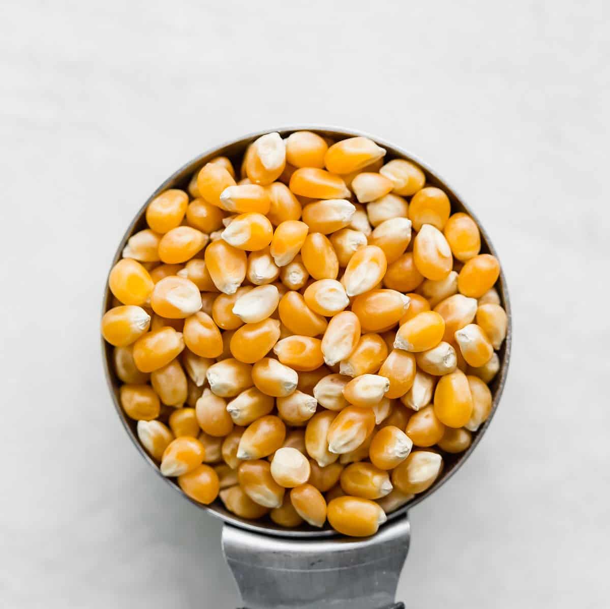 Popcorn kernels in a metal cup on a white background. 