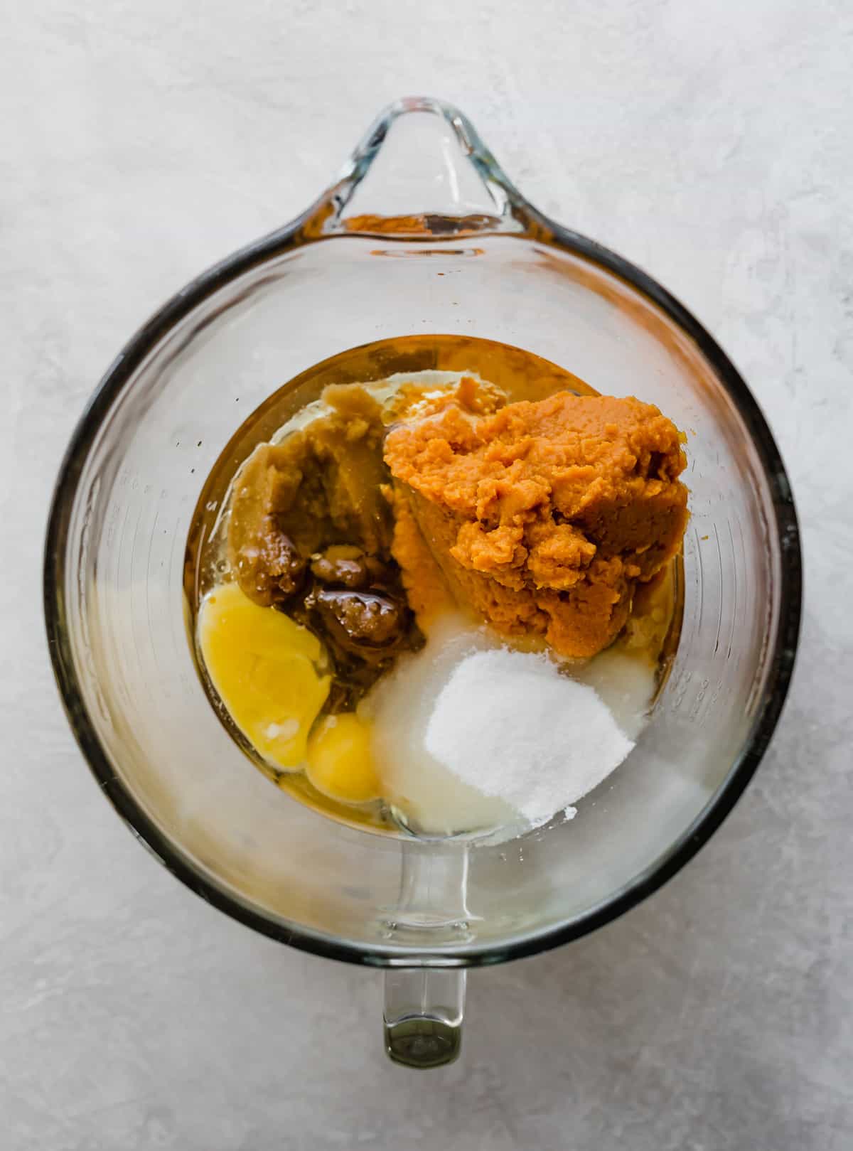 A glass mixing bowl with pumpkin cake ingredients in it.