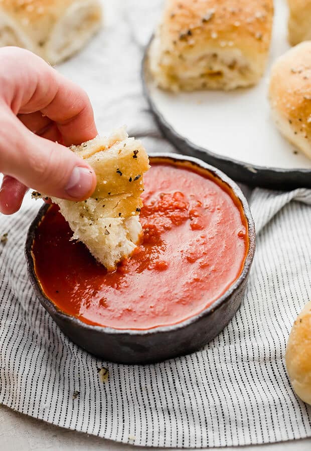 A hand dipping a pizza roll in a bowl of pizza sauce.
