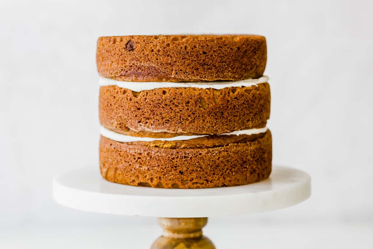 Three Pumpkin Cake layers on a cake stand with cream cheese frosting between each layer. 