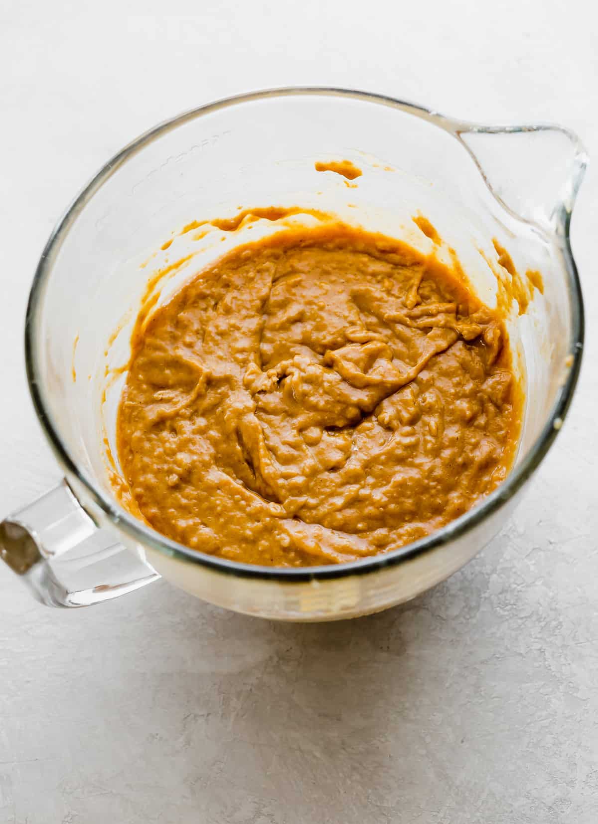 Pumpkin Cake batter in a glass mixing bowl on a white background.