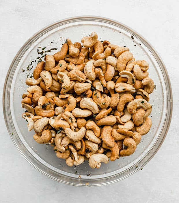 Roasted cashews tossed in a glass bowl of fresh rosemary, melted butter, and spices.