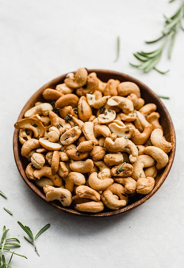 A plate of rosemary cashews surrounded by fresh rosemary sprigs.