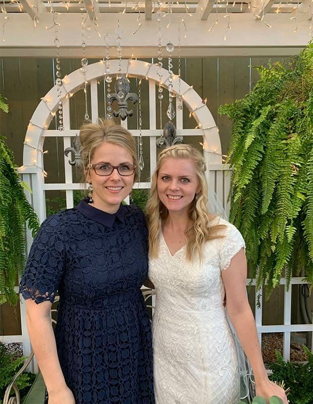 A bride in a white dress standing next to a woman with glasses wearing a navy dress.