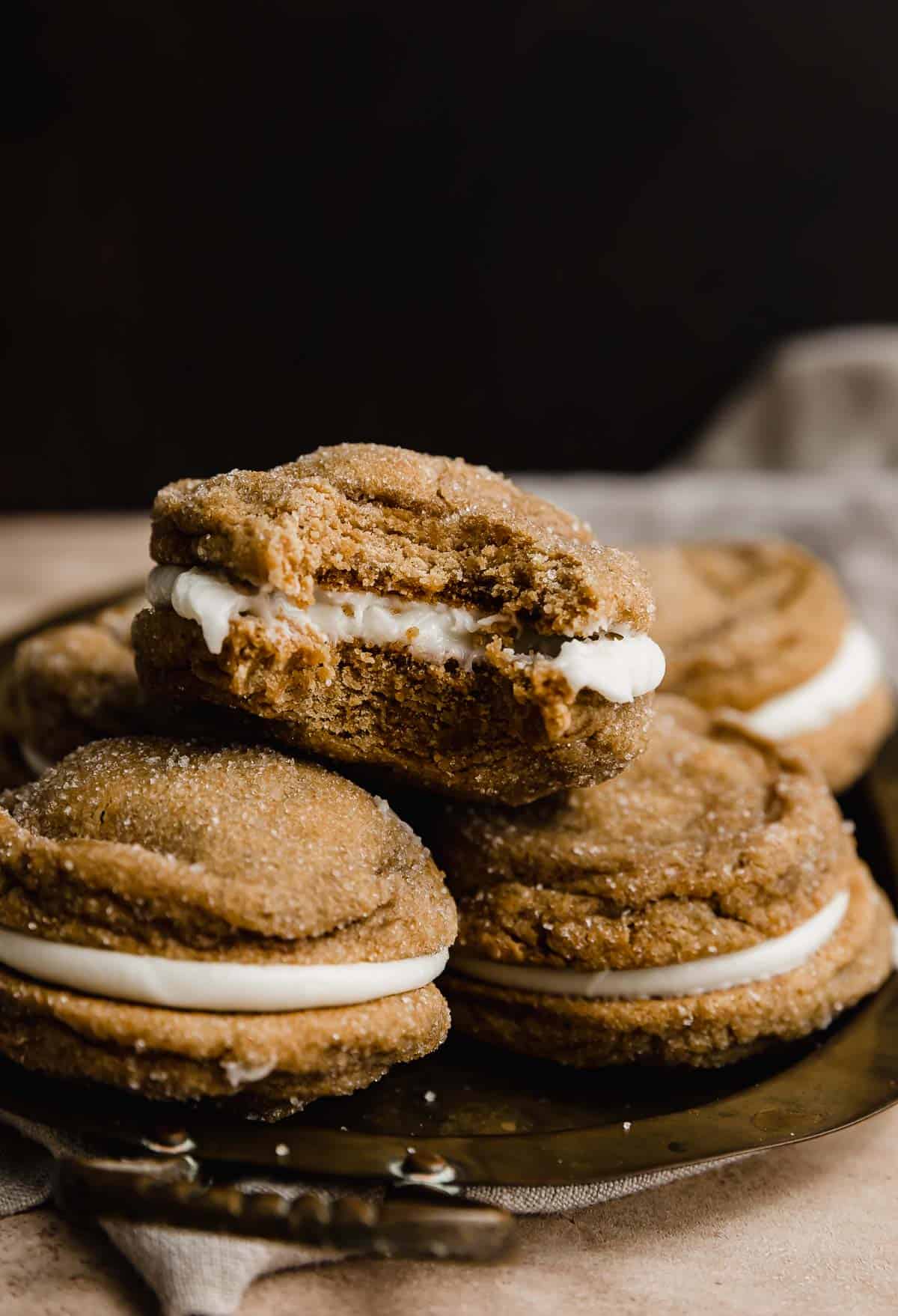 Gingerbread Sandwich Cookies with a bite taken out of one, that's against a dark brown background.