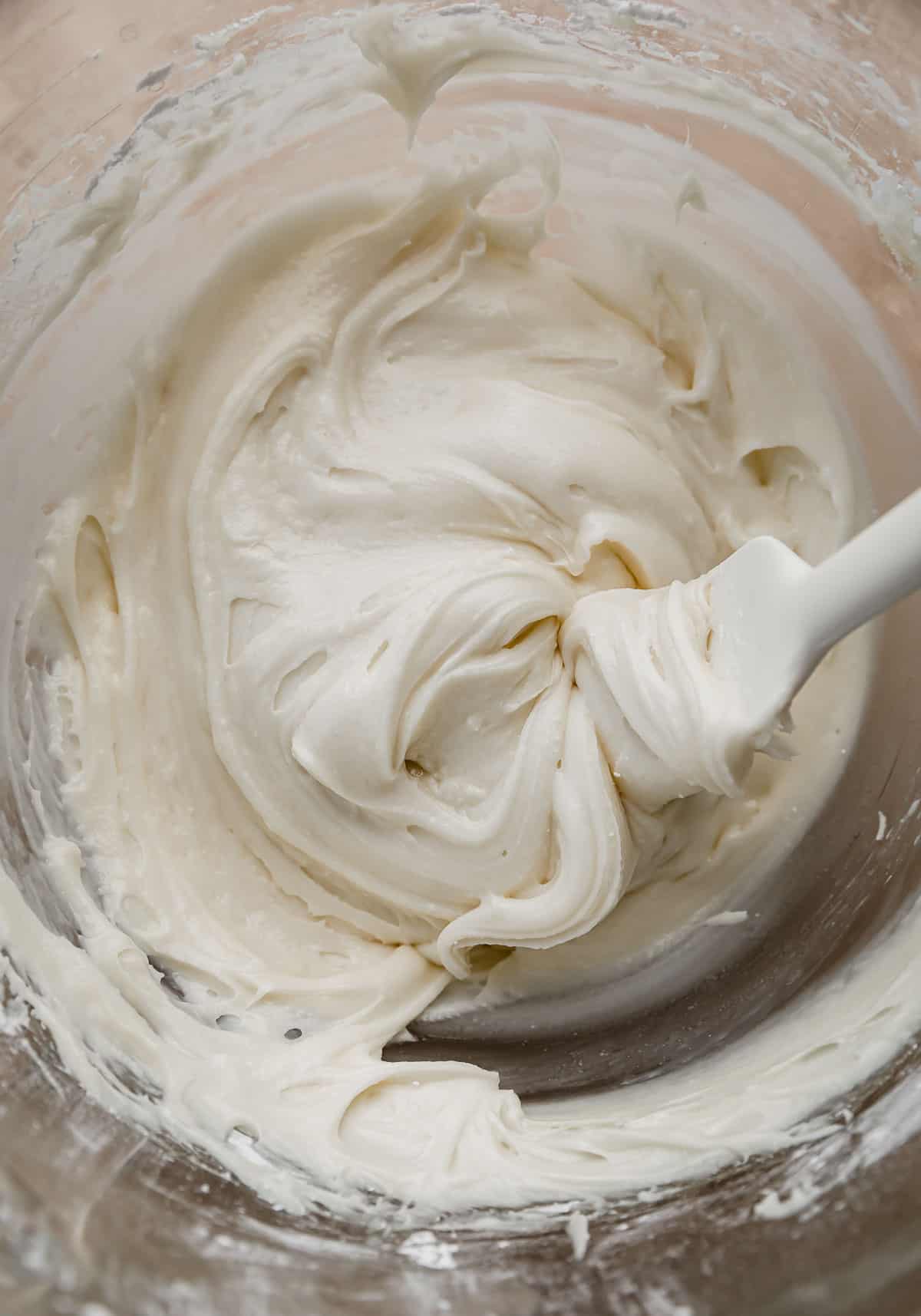 White cream cheese frosting used in the center of Gingerbread Sandwich Cookies (or gingerbread whoopie pies) in a glass bowl.