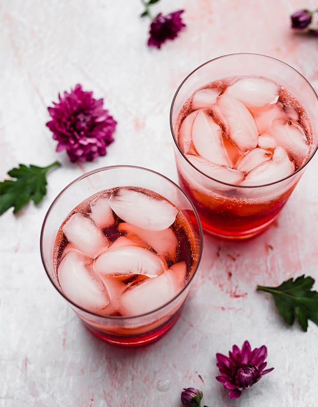 Two glass cups full of ice, club soda, and raspberry syrup flavoring.