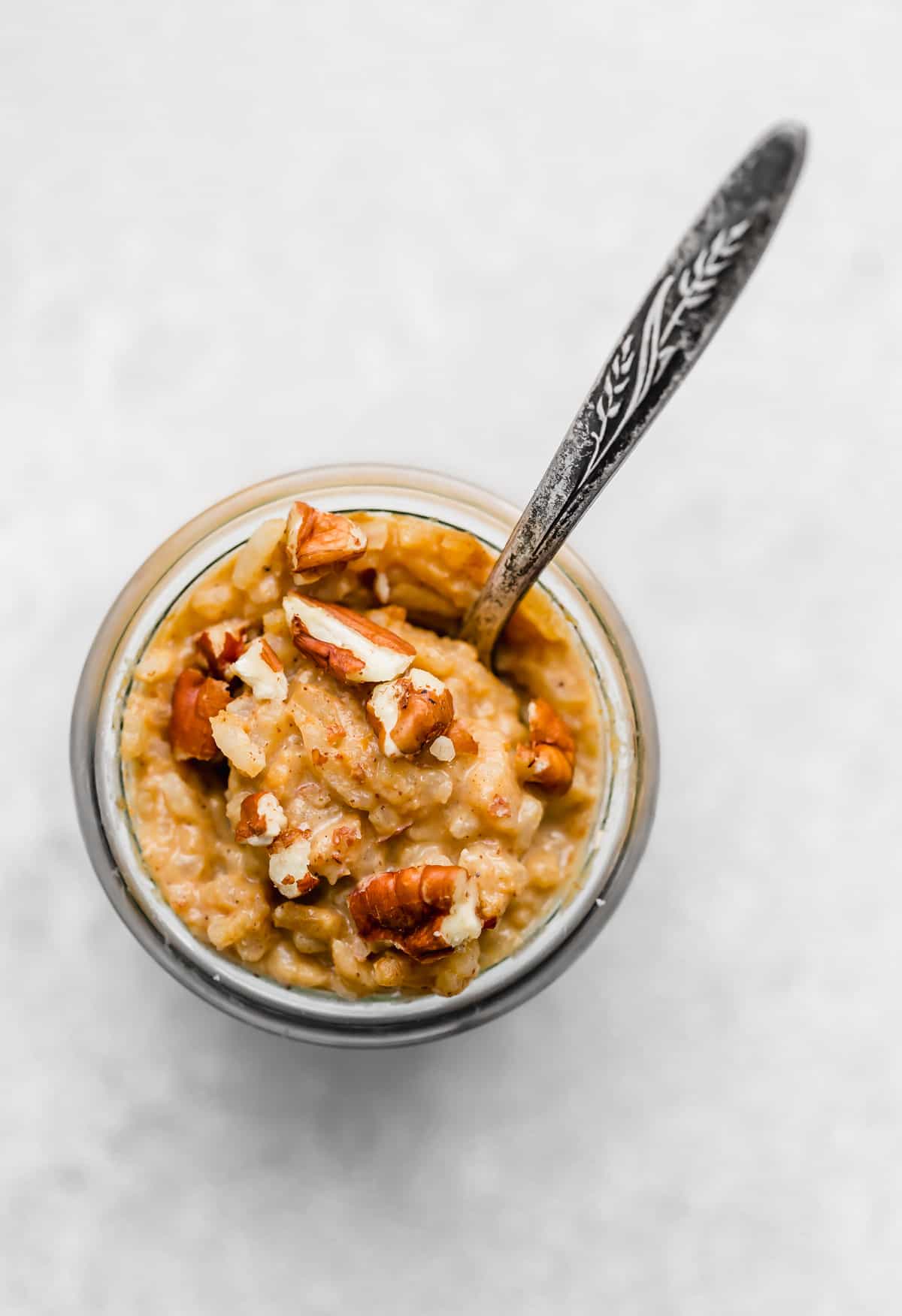 Overhead photo of Pumpkin Rice Pudding in a glass jar that is topped with chopped pecans.