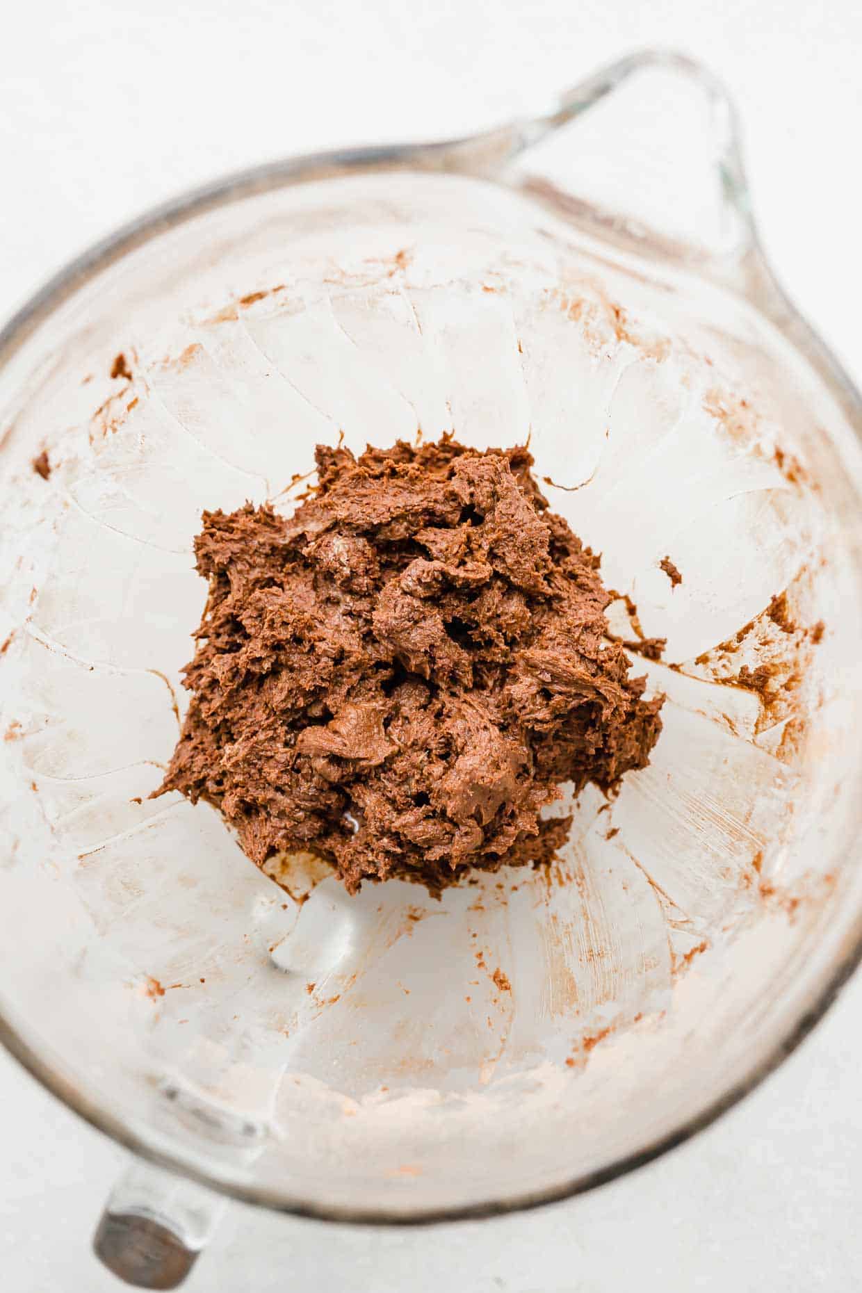 Brown chocolate turtle cookie dough in a glass mixing bowl on a white background.