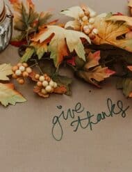 Leaves on a table with "give thanks"written on the tablecloth.