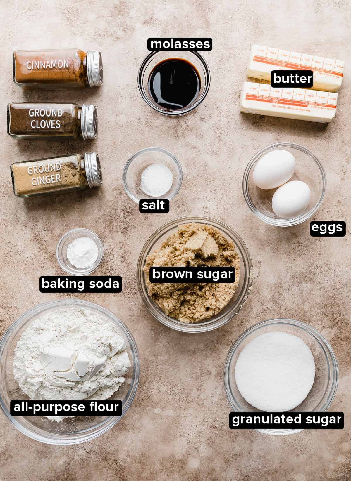 Gingerbread Sandwich Cookies ingredients portioned into glass bowls on a light brown textured background.