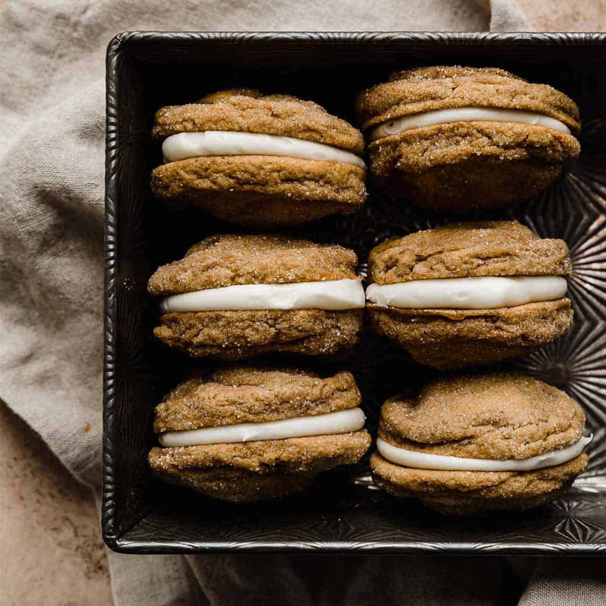 Six gingerbread sandwich cookies (or gingerbread whoopie pies) with a cream cheese filling, stacked on top of each other in a baking dish.