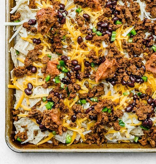 A baking sheet with loaded nachos, prior to baking.