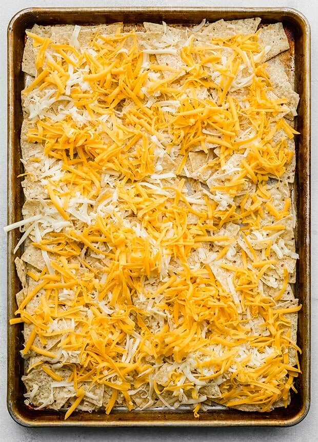 A baking sheet covered in tortilla chips and shredded cheese.