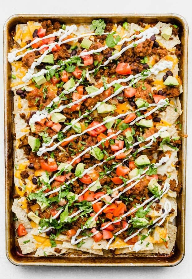 An overhead photo of a baking sheet full of loaded nachos, garnished with cilantro and sour cream.