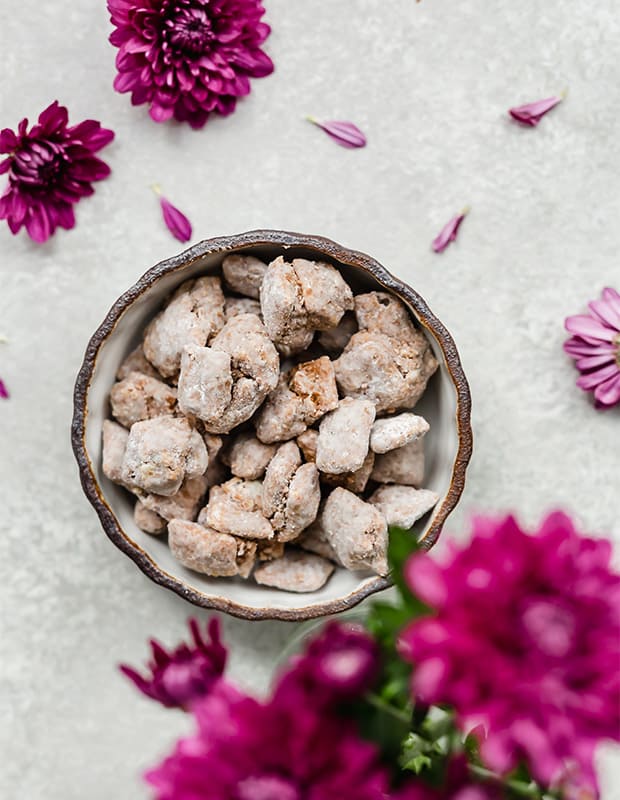 A bowl of muddy buddies surrounded by purple flowers.