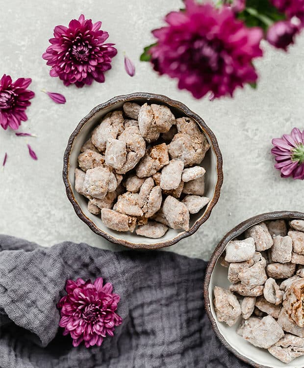 A bowl of muddy buddies surrounded by purple flowers.