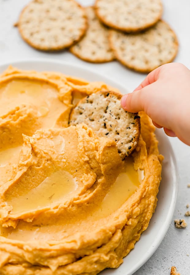 A cracker dipping into Sweet Potato Hummus.