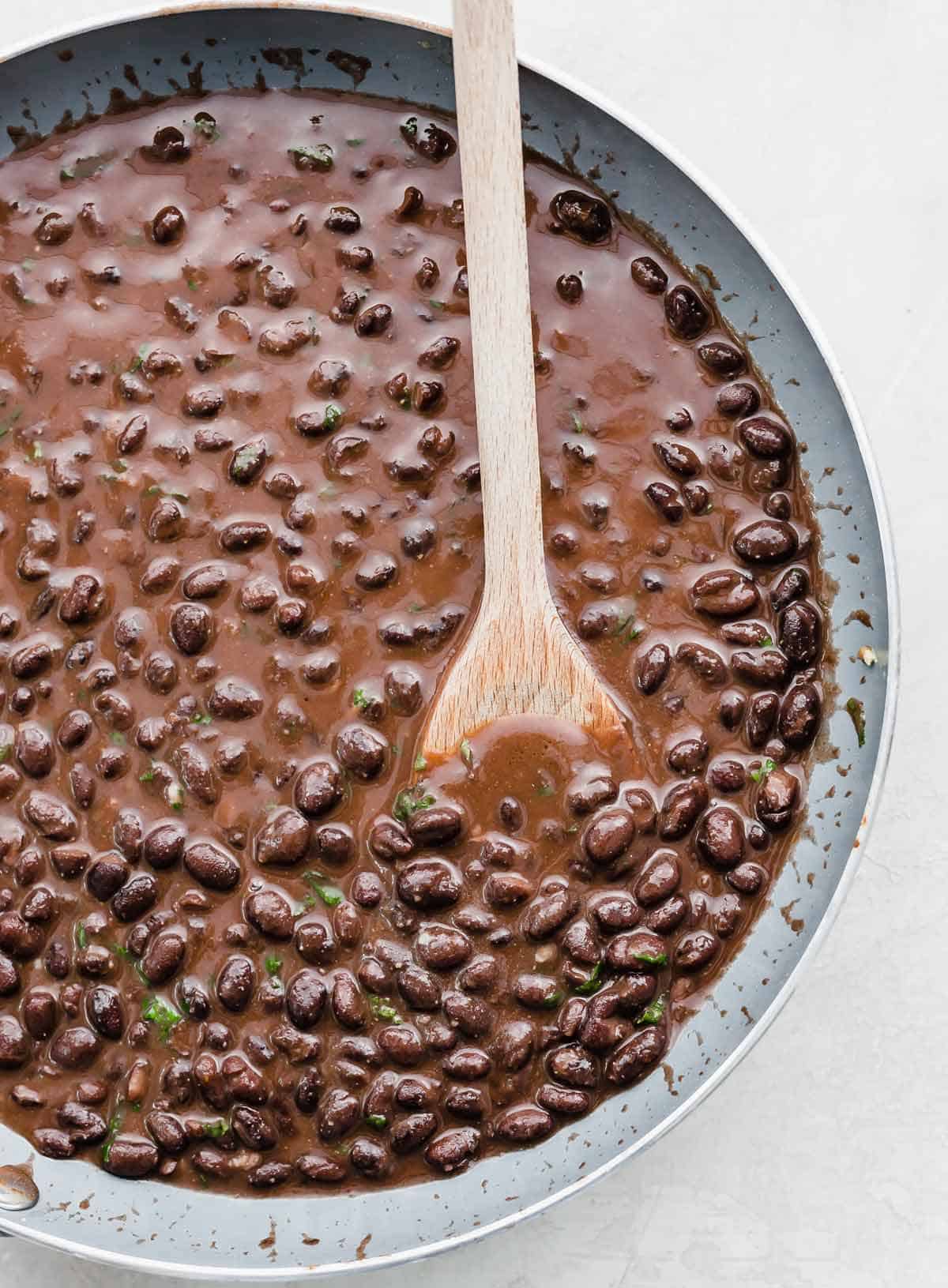 A wooden spoon in a skillet filled with Cafe Rio Black Beans.