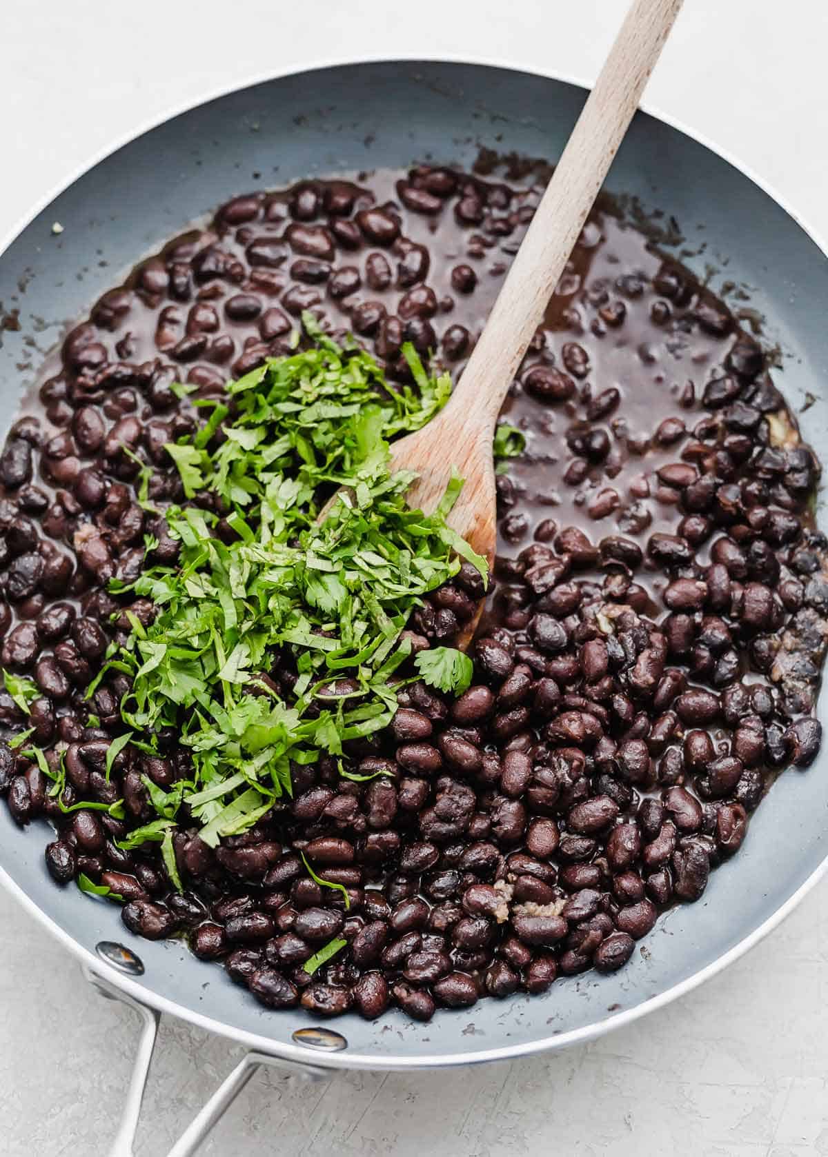 Chopped cilantro on top of black beans in a gray skillet.