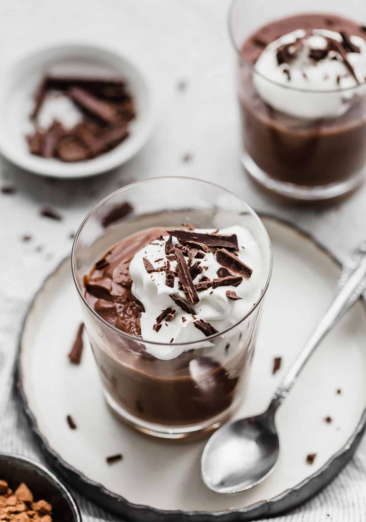 Homemade Chocolate Pudding in a glass cup on a white plate with a spoon on the plate.