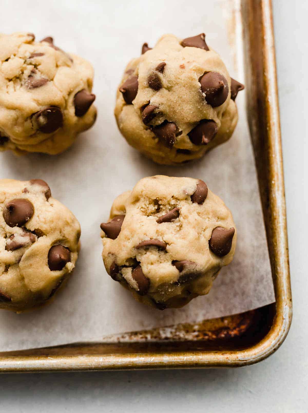 Crumbl Chocolate Chip Cookie dough balls on a parchment lined baking sheet.