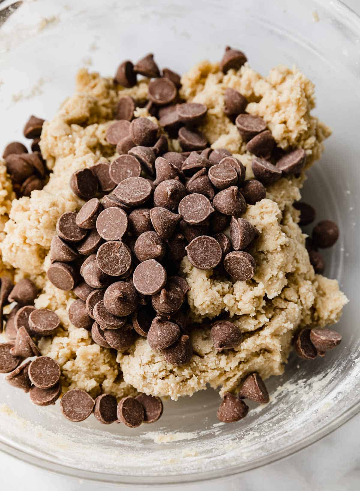 Milk chocolate chips overtop homemade Crumbl chocolate chip cookie dough in a glass bowl.